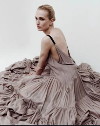 Model seated on the floor wearing a gathered taupe dress against a white background
