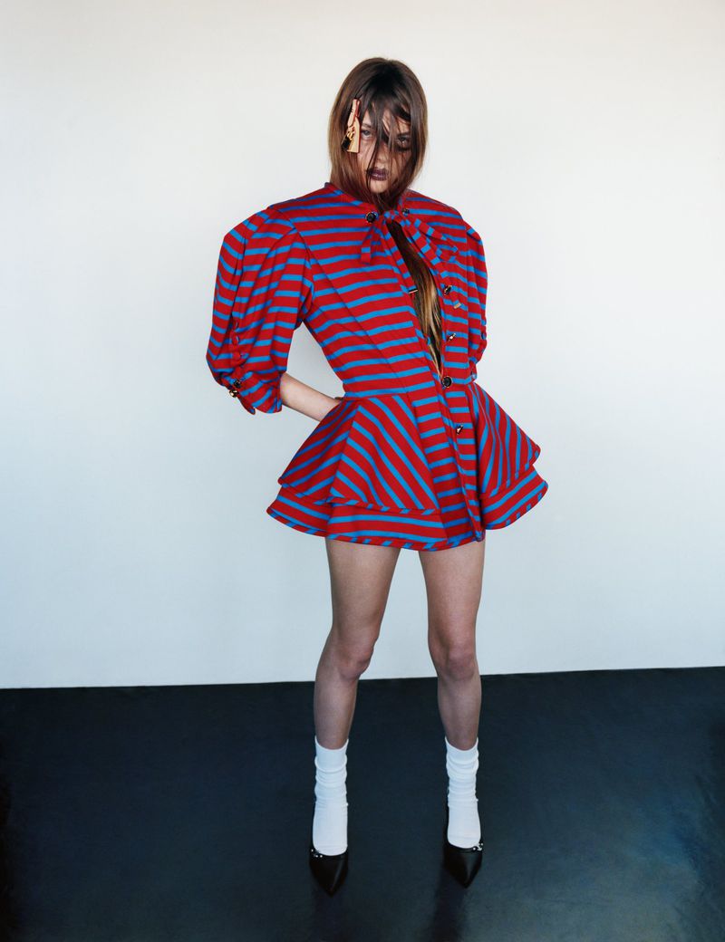Fashionable adult woman in a red and blue striped dress with white socks and black heels posing in front of a white background.