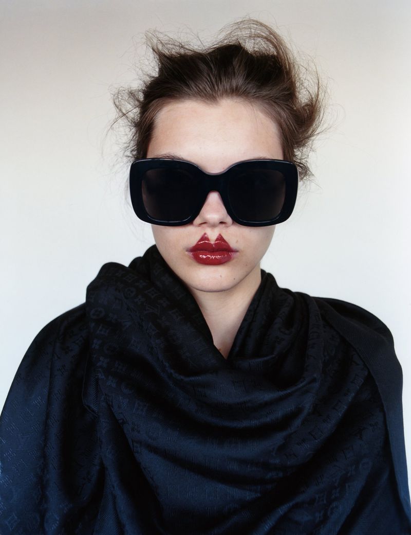 Portrait of a woman wearing sunglasses and black shawl. Dark red lipstick art on lips. Studio lighting, neutral background. Fashion, beauty.