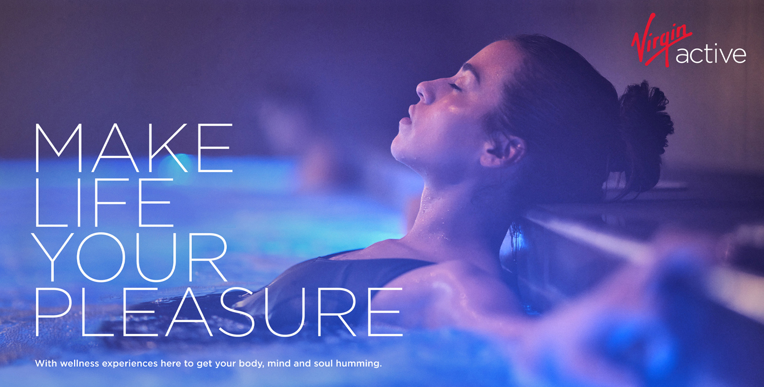 Woman relaxing in pool, eyes closed, in a serene spa setting with mood lighting. Wellness concept with 'Virgin Active' logo.