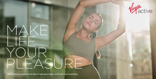 Woman in a green sports bra stretching her arms overhead in a bright sunlit fitness space for Virgin Active