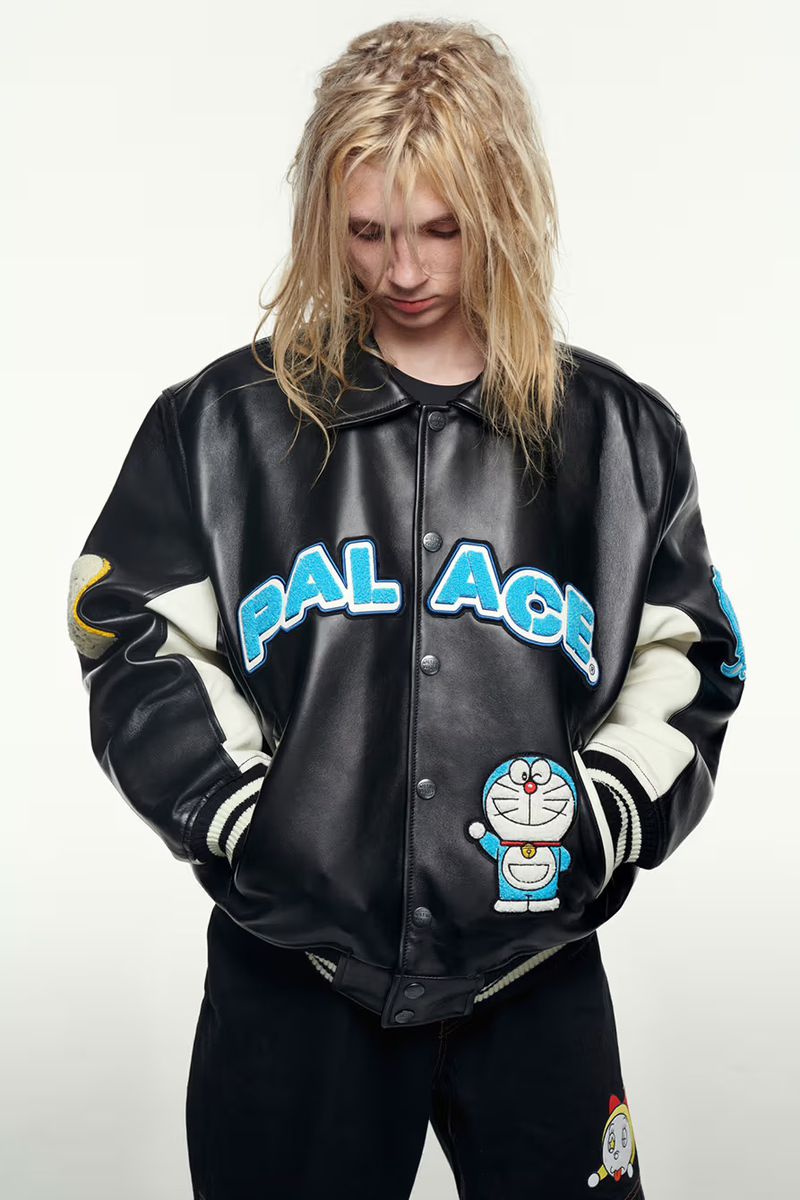 A fair-skinned young adult with long blonde hair poses in a black leather jacket with blue lettering against a white background.