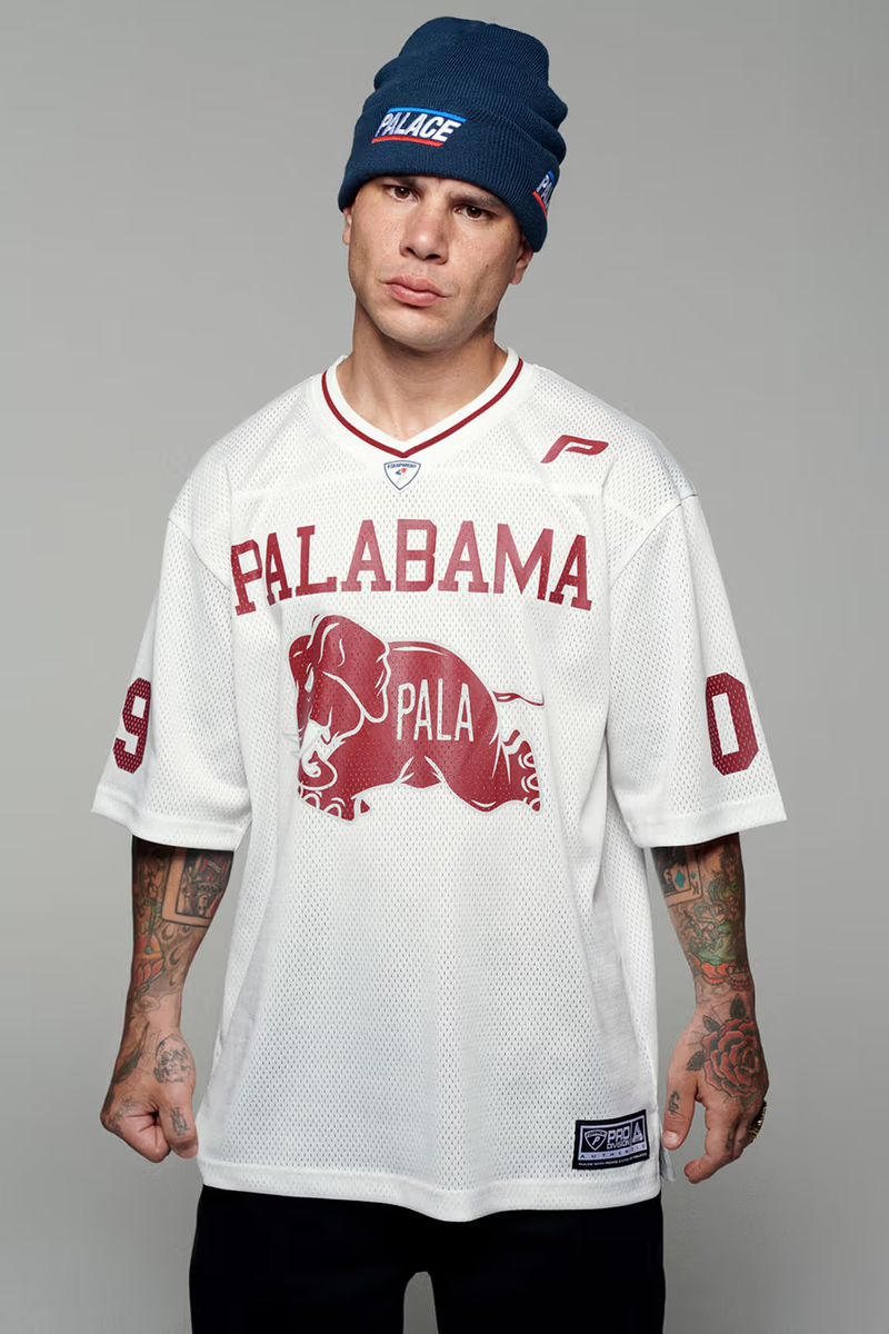 A man in a blue beanie and a white jersey with a graphic of an elephant stands indoors against a neutral background.