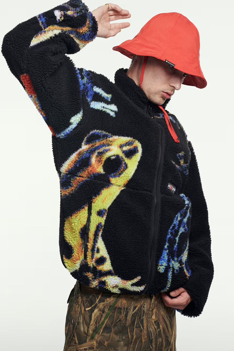 Man in patterned fleece jacket and red bucket hat posing against a white backdrop in a studio setting.