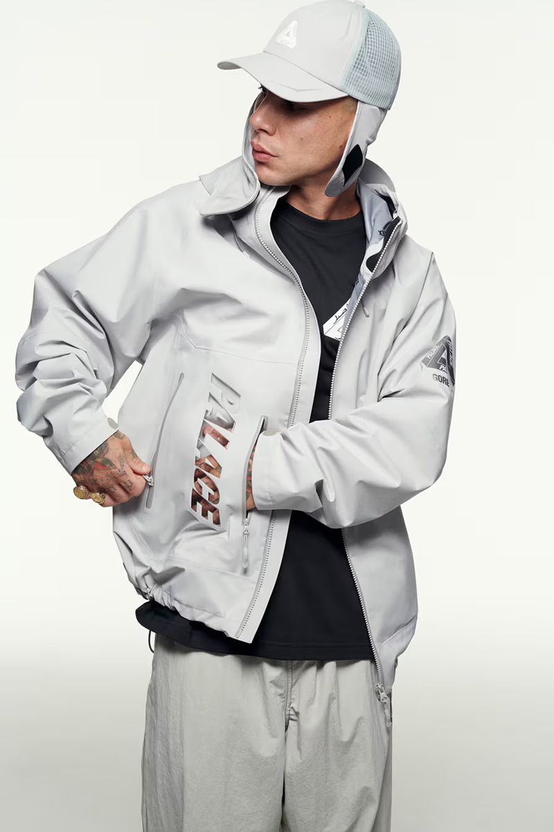 Fashion shot of a man in a light gray jacket and pants, wearing a matching cap against a clean white background in a studio.