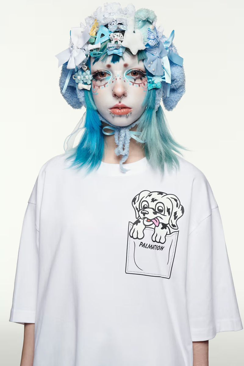 Portrait of a young woman with unique makeup and hair wearing a white t-shirt with a Dalmatian graphic on a white background.