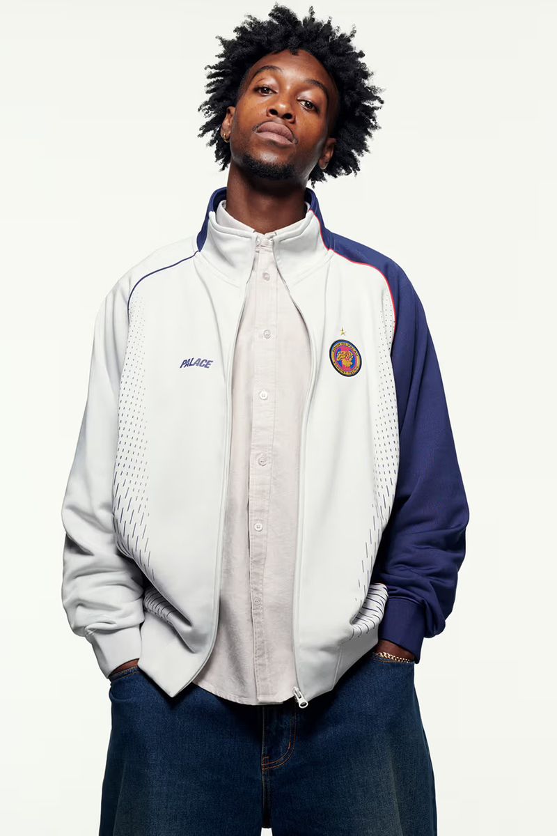 A male fashion model with an afro poses against a plain white background wearing a two-tone Palace jacket and blue jeans.