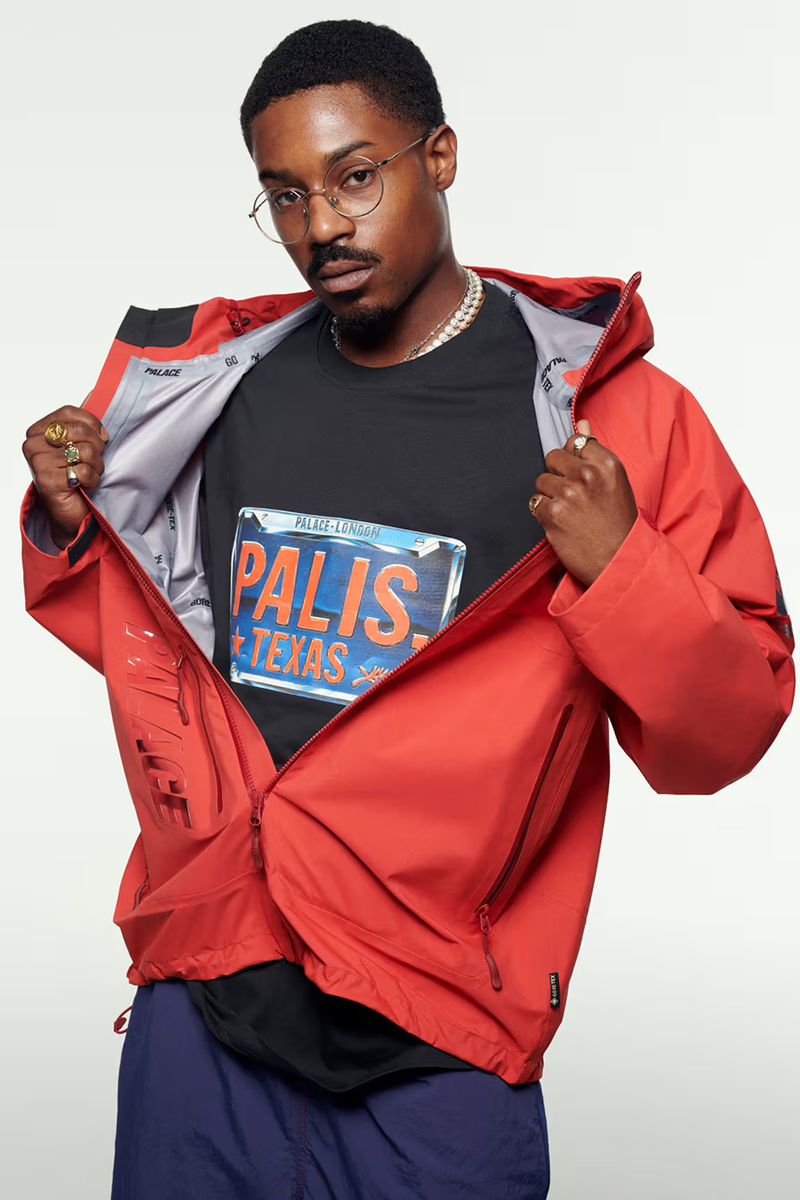 Stylish African American man in a red jacket and graphic tee poses against a white backdrop, showcasing modern urban fashion.