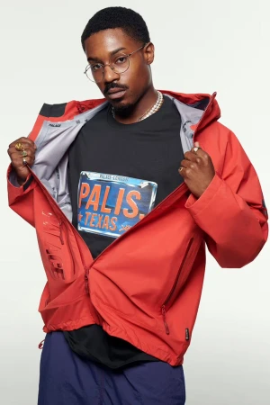 Stylish African American man in a red jacket and graphic tee poses against a white backdrop, showcasing modern urban fashion.
