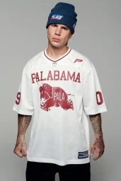 Man wearing a blue beanie and white sports jersey with red lettering standing against a plain grey background