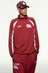 Man wearing a maroon track jacket, matching track pants, and a baseball cap against a plain white background.