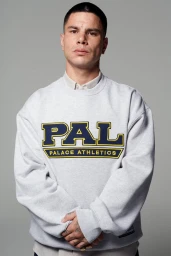 Man wearing a grey crewneck sweatshirt with bold yellow and blue lettering against a neutral grey studio background