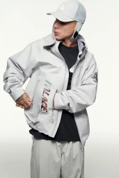 Model wearing a light grey Palace technical zip jacket, matching trousers, and a cap with ear flaps against a white background.