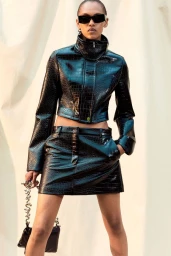 Model in black textured leather jacket and matching mini skirt wearing sunglasses against a neutral backdrop for Sportmax Resort 2026