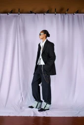 Model Bebe Parnell wears a pinstripe blazer and wide cuffed denim trousers against a draped lilac backdrop for Sportmax.