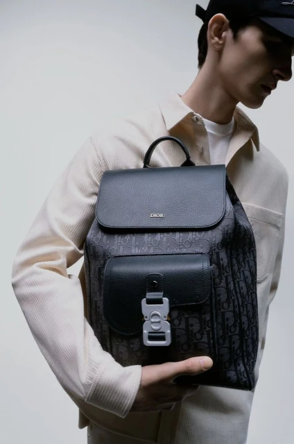 Model showcases a Dior backpack in a studio setting, highlighting the bag's design and details. The photograph focuses on fashion.