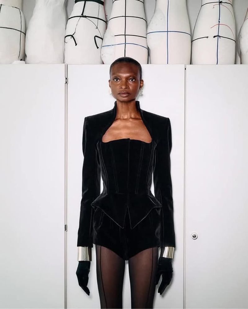 Elegant Black fashion outfit on a slender African American woman posing indoors against a white wall with fashion design forms.