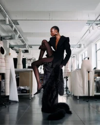 Model Debra Shaw posed in a black blazer and sheer stockings in a Parisian atelier for Mugler Fall 2025.