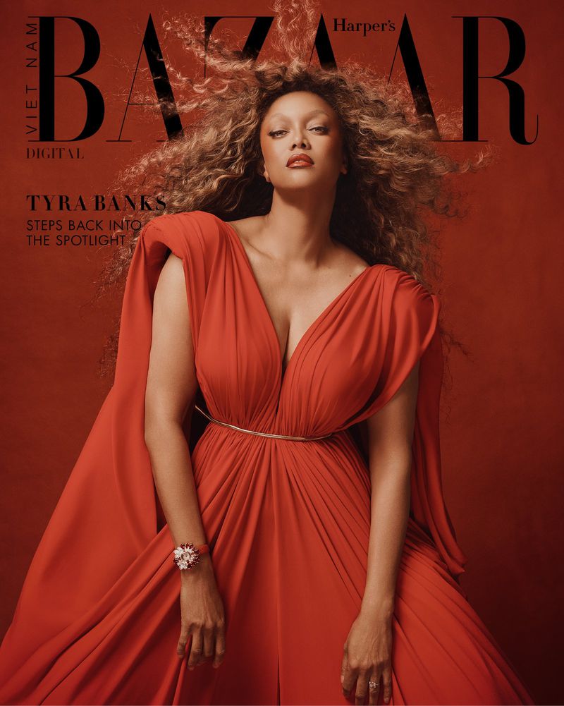 Tyra Banks on the cover of Harper's Bazaar Vietnam. She is wearing a red dress with gold belt and has big hair and makeup.