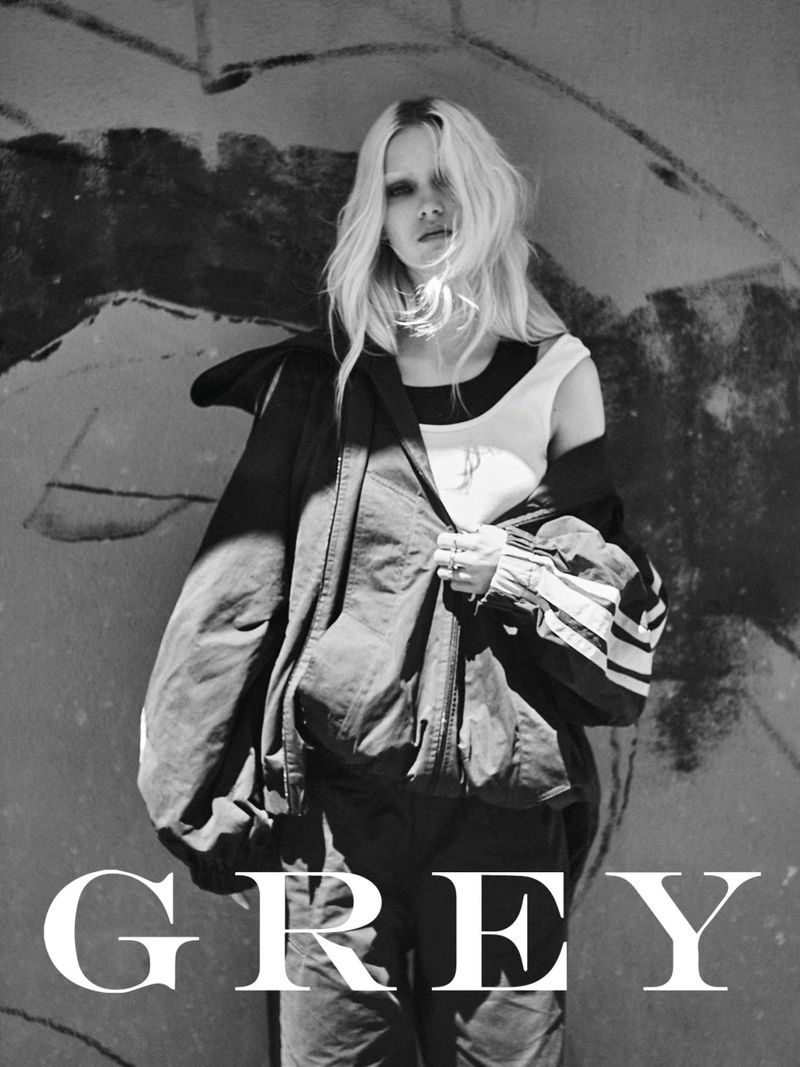 Black and white portrait of a model posing in front of an abstract painted wall, wearing casual clothing with an oversized jacket.