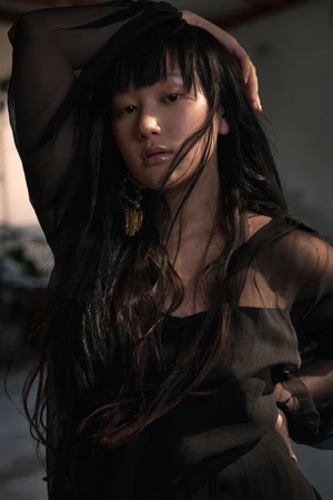 Portrait of a woman with long dark hair wearing a sheer black top posing for Russh Magazine.