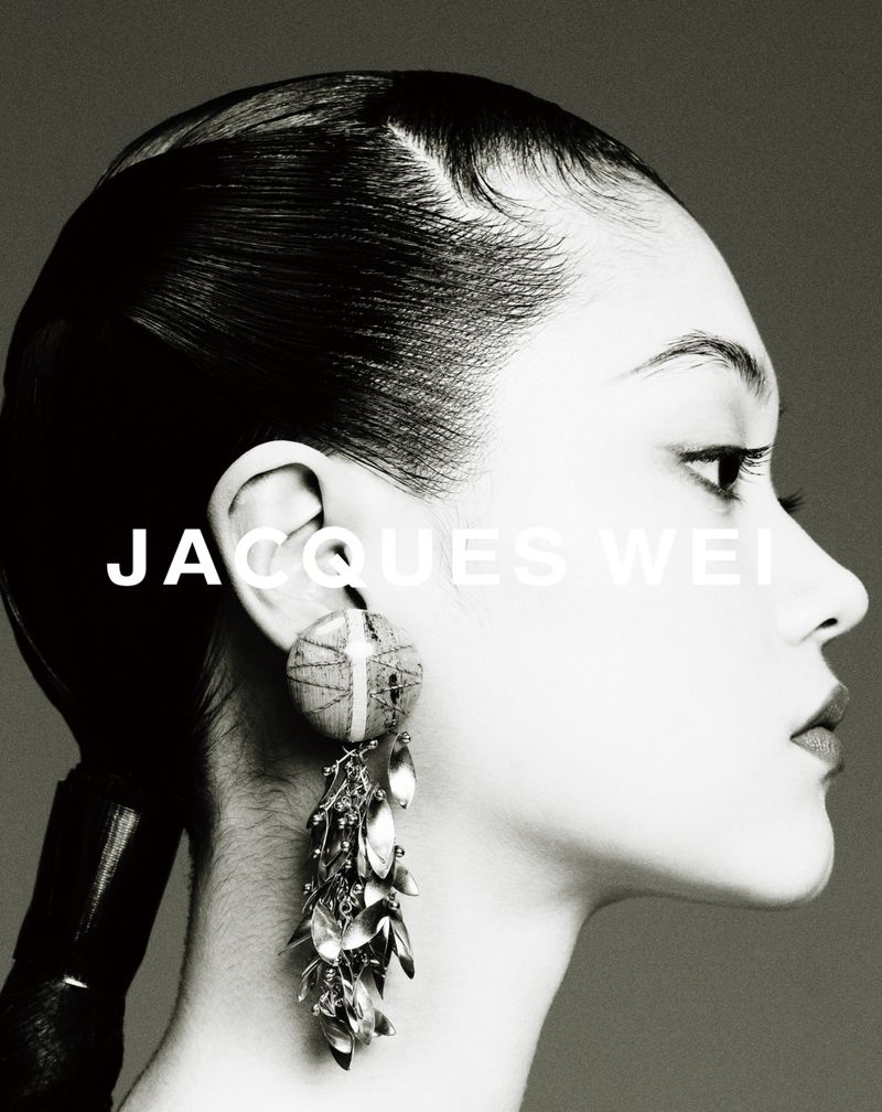 Monochrome portrait of a woman with side profile, elegant earrings, and sleek hair against a dark background in a studio setting.