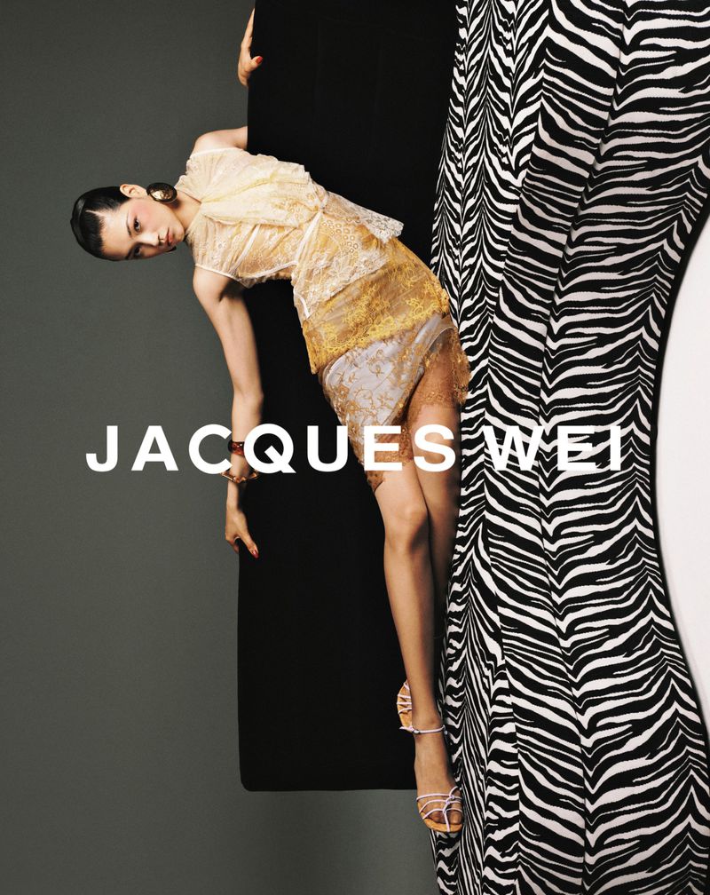 Fashion shot featuring a model in a gold dress, posing near black and zebra-striped columns, against a gray background with text.