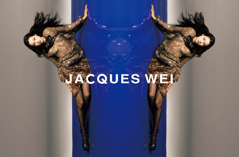 Two mirrored women in sheer tops and leopard print skirts pose against a blue wall with text overlay, high heels, dark hair.
