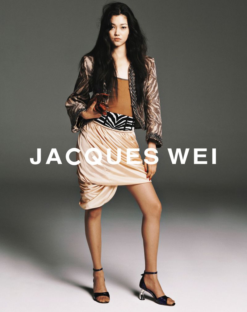 Fashion shot of a young Asian woman in a jacket and skirt, posing indoors against a grey background, with Jacques Wei text overlay.