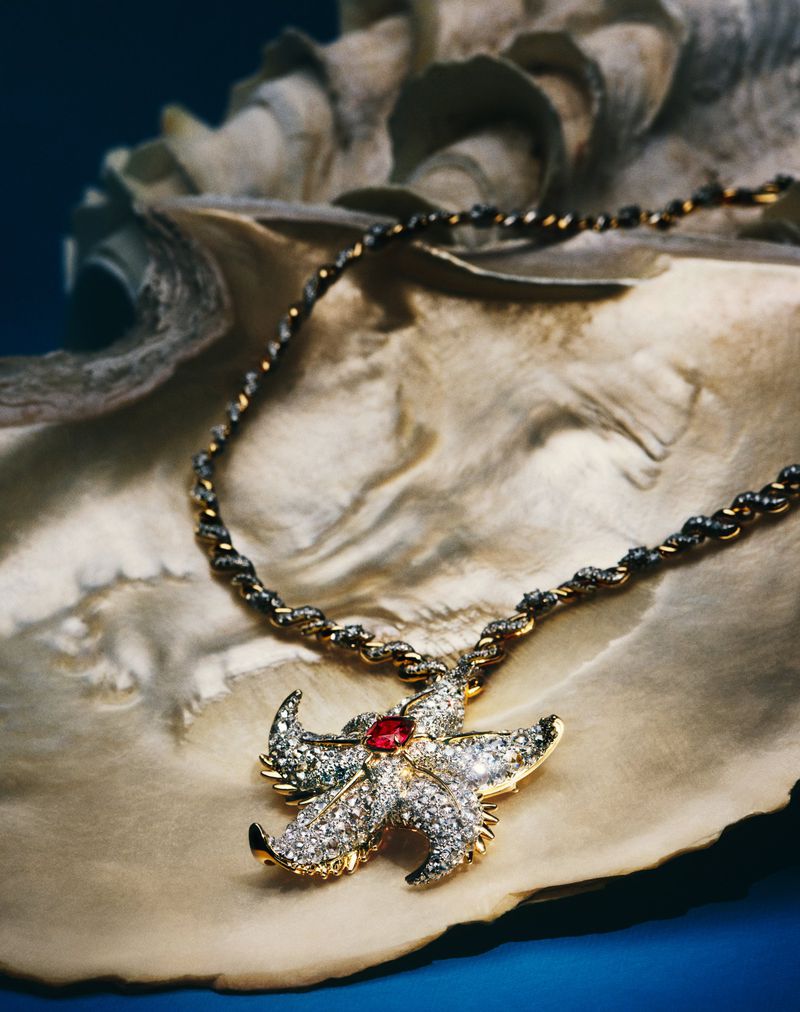 Elegant gold necklace with a starfish pendant set against a giant clam shell, presented on a vibrant blue backdrop.