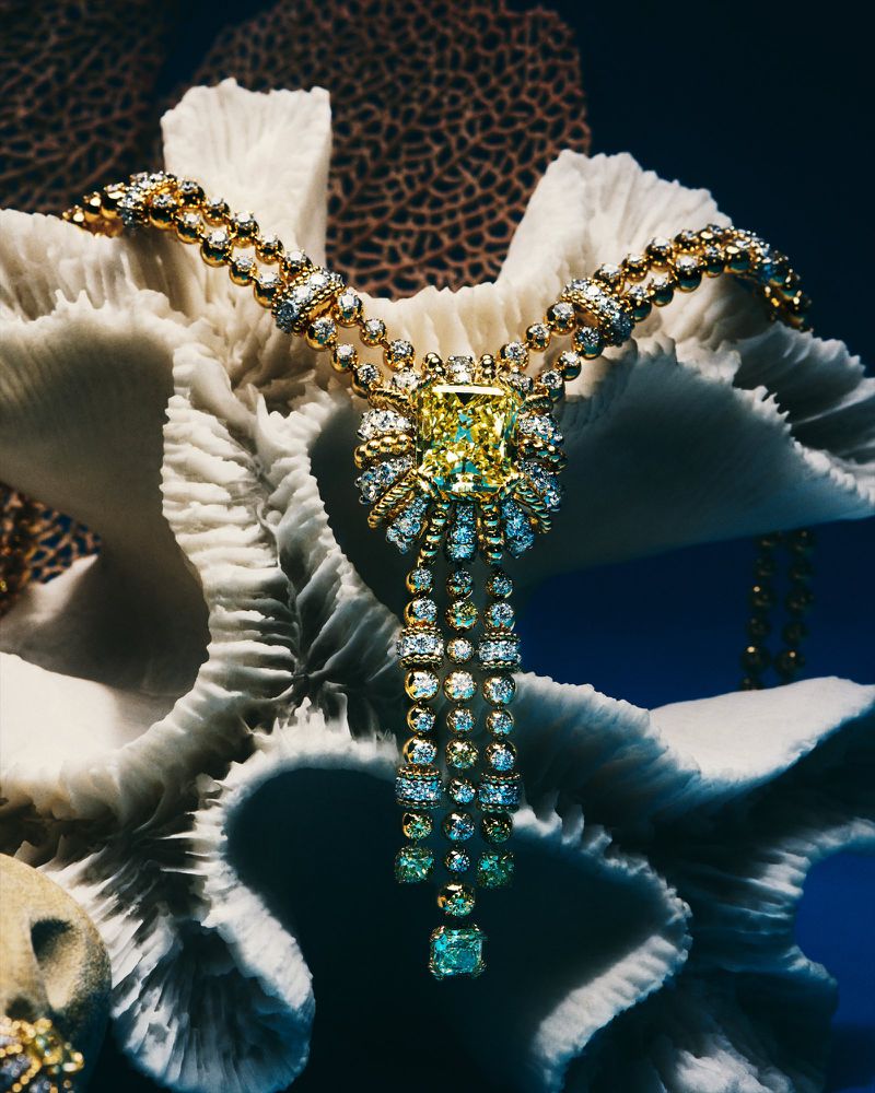 Close-up of a diamond necklace with yellow central stone, showcased on textured white coral against a dark blue background.