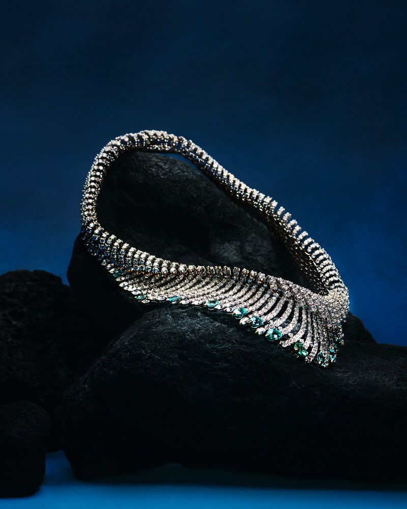 Diamond and emerald necklace on a black textured surface against a dark blue backdrop, jewelry, fine gems, luxury.