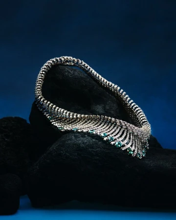 Diamond and emerald necklace on a black textured surface against a dark blue backdrop, jewelry, fine gems, luxury.