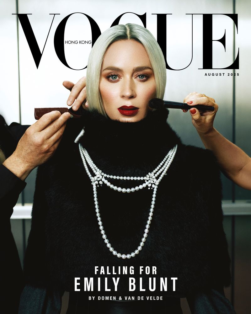 Emily Blunt on Vogue Hong Kong, August 2025 issue, wearing a black top and pearl necklace, with makeup artists applying cosmetics.
