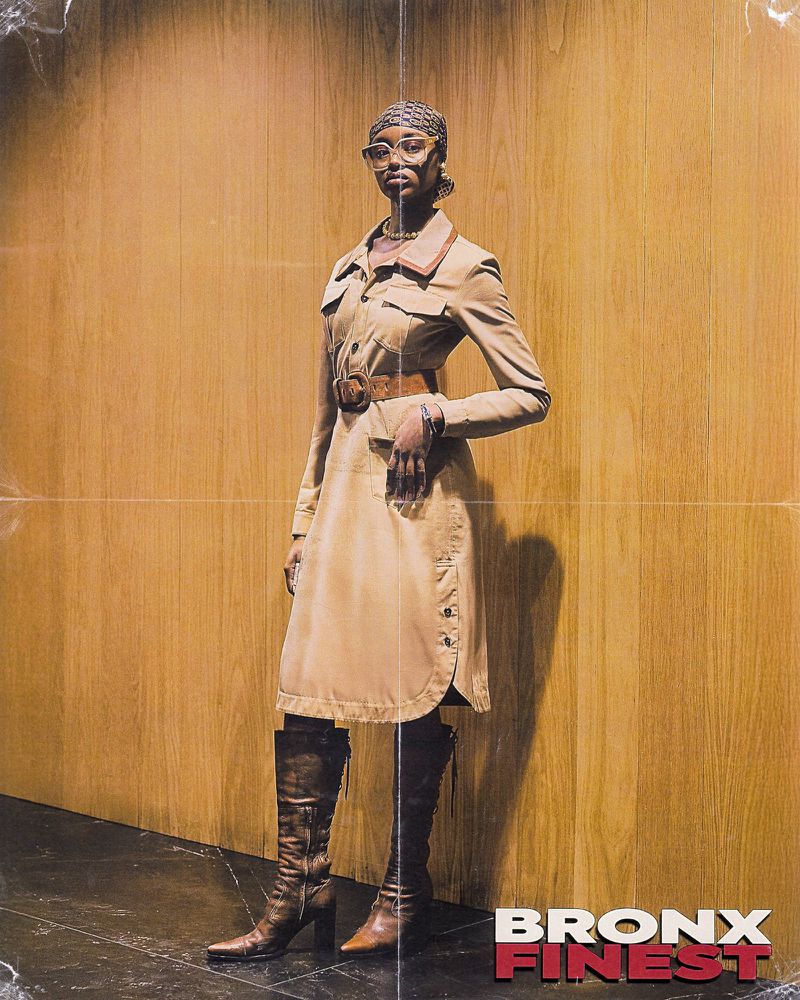 Fashionable woman in vintage tan dress, headscarf, and boots poses against a wood wall in a studio setting. Editorial fashion shot.