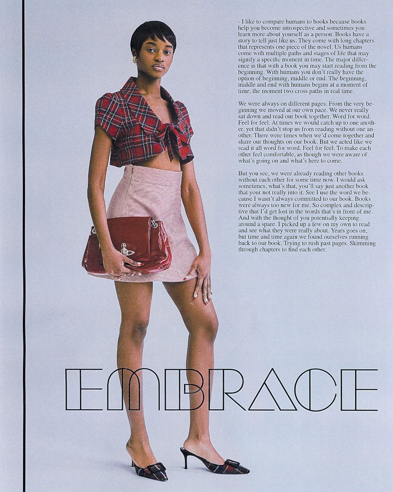 A full-length shot of an adult woman in a red and black plaid crop top and light pink miniskirt, holding a red patent handbag, in a studio setting.