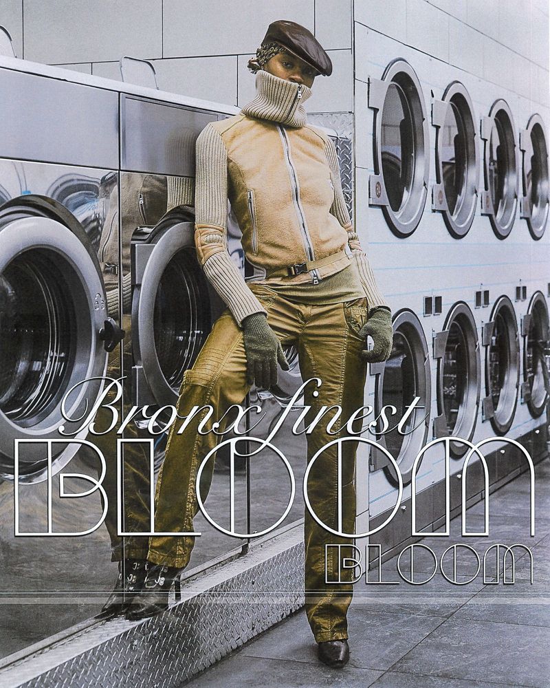 A woman wearing olive-toned pants and jacket with a wool turtleneck poses in front of commercial washing machines for a fashion editorial.