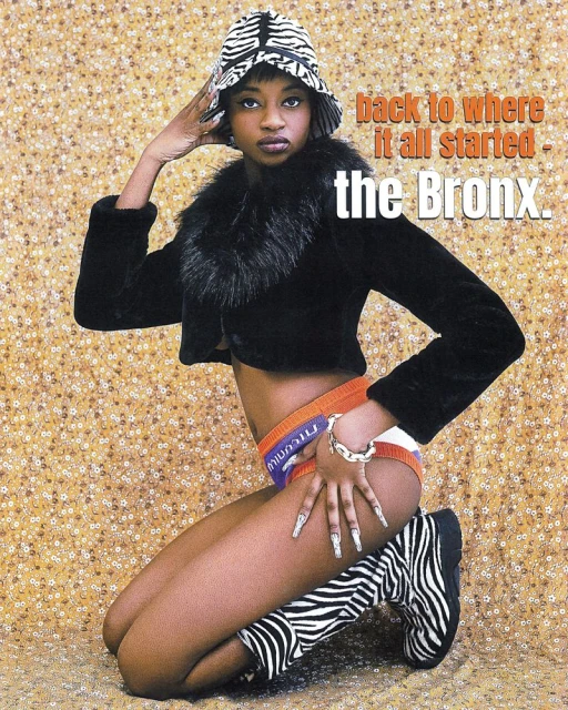 Young woman poses kneeling indoors with a zebra-print hat and boots, black fur-trimmed jacket, and visible undergarment waistband. 