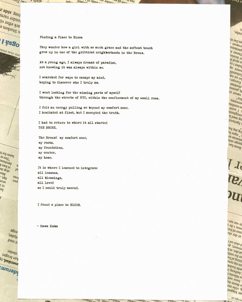 Poem typed on white paper in a serif font. The paper sits on newspaper print with cream and dark gray hues in indoor setting.