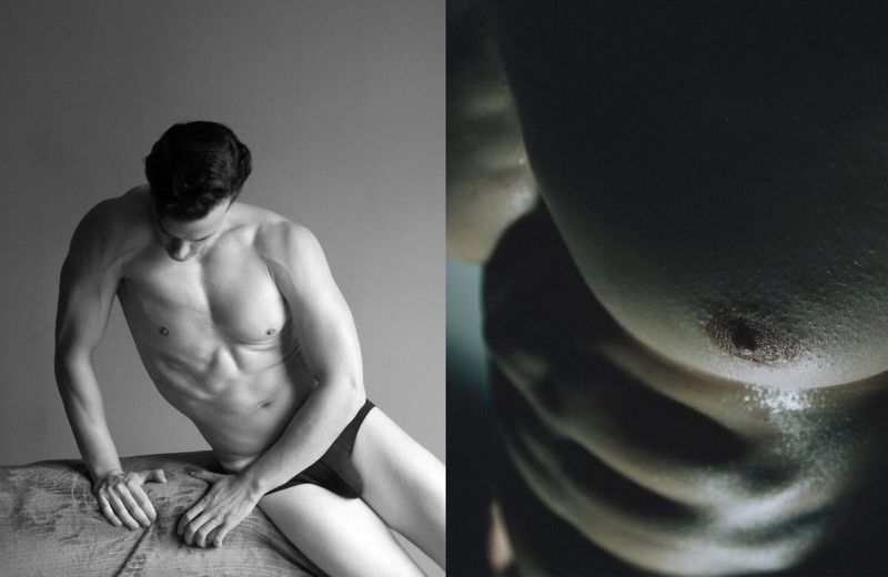 Black and white artistic shot of a muscular, shirtless man with dark hair reclining indoors, showcasing toned physique in studio lighting.
