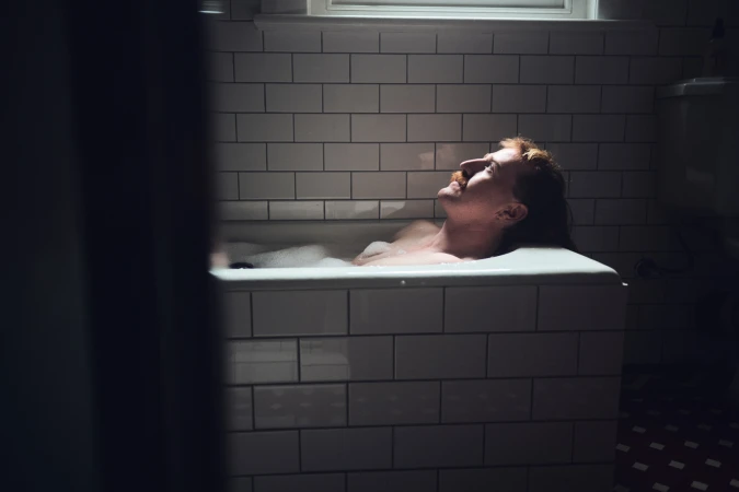 Man with a mustache relaxing in a bathtub inside a tiled bathroom for Movember