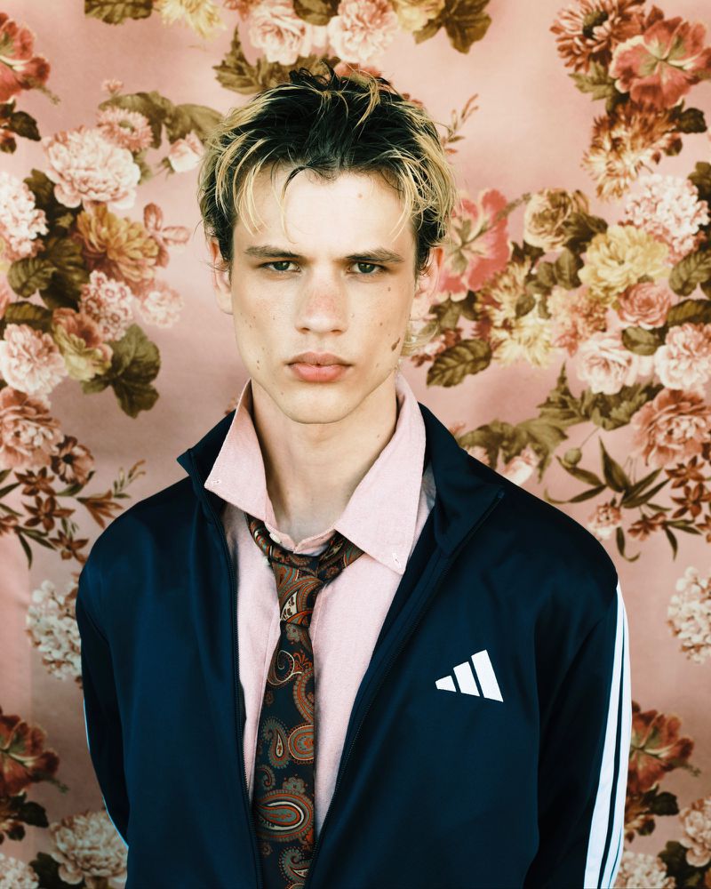 Model Lazar Dedic in a track jacket, pink shirt, and paisley tie against a pink floral background.