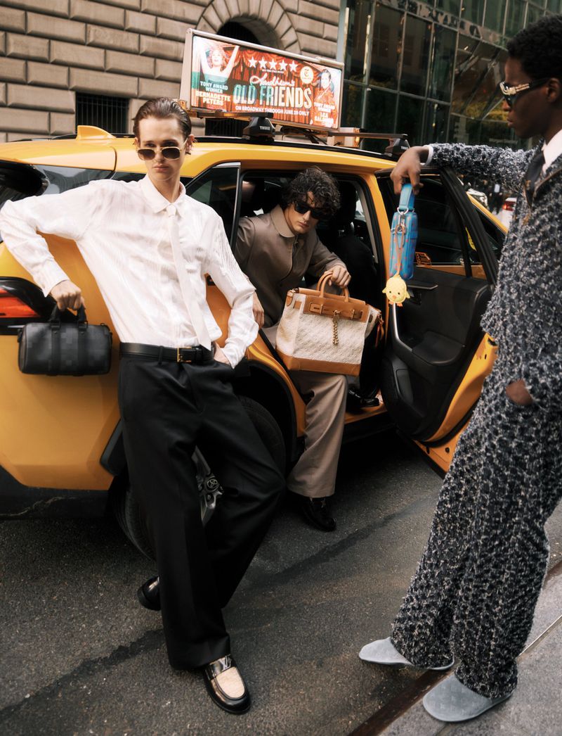Three stylish adult men pose near a yellow New York City taxi, showcasing high-fashion suits and carrying luxury handbags in an urban setting.