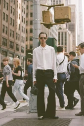 Man wearing a white shirt and dark trousers standing by a street pole amid city pedestrians