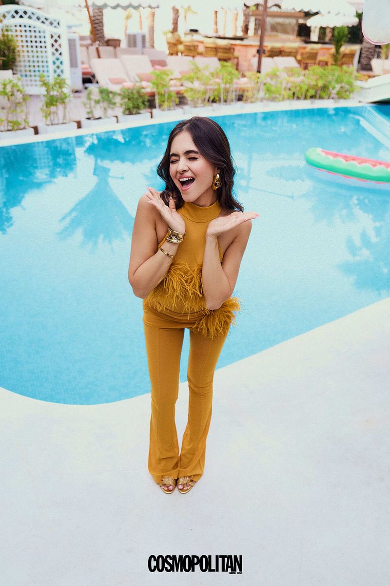 Young woman in yellow outfit poses near pool with inflatable watermelon in outdoor setting, shot by Cosmopolitan magazine.