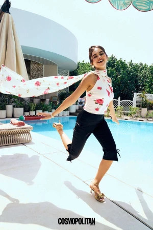 A vibrant fashion editorial captures a young adult woman in motion outdoors, wearing a floral top and black capri pants near a pool.