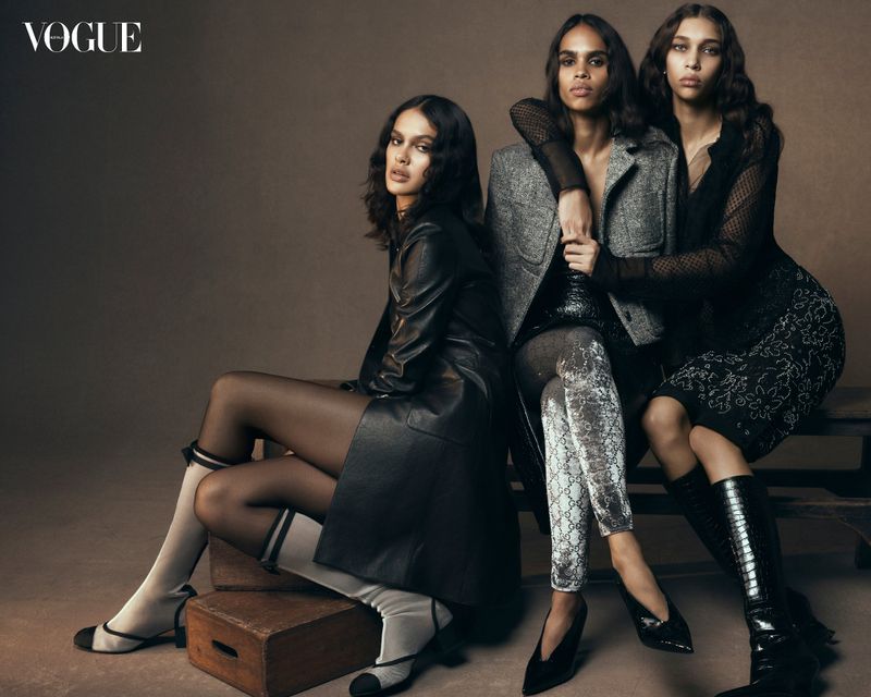 Fashion editorial shot of three female models in fashionable dresses and jackets posing in front of a studio background.