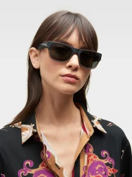 Model wearing dark framed sunglasses and a patterned shirt against a plain white background for DKNY