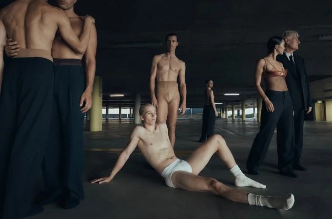 Artistic shot of diverse group of people in an underground parking lot; some shirtless, some in business suits, and some in dancewear.