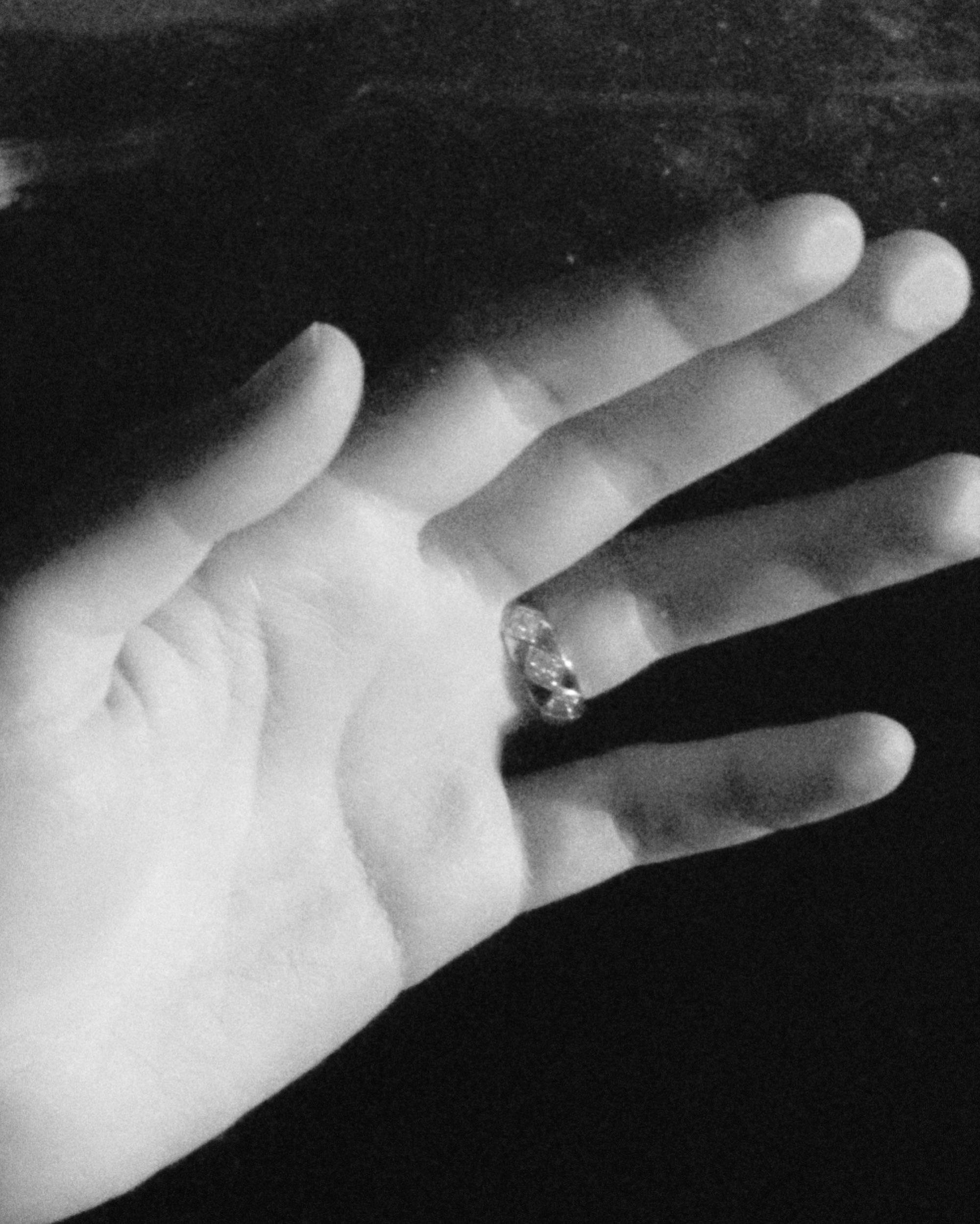 Close-up monochrome image of a hand wearing a diamond ring on a dark background